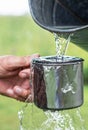 Man is holding a steel mug and a well water is pouring from a bucket Royalty Free Stock Photo