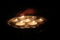 Man holding tealight wax candles or diya lamp in hand in dark night.