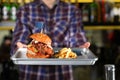 Man holding tray with delicious burger and french fries indoors