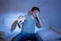 Man holding tv remote control sitting at living room couch watching television blocking his eyes Royalty Free Stock Photo