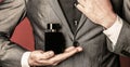 Man holding up bottle of perfume. Men perfume in the hand on suit background. Fragrance smell. Fashion cologne bottle Royalty Free Stock Photo