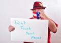 A man holding up a sign `Don`t tourch your face` and rubbing his eye