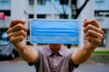 Man holding up surgical mask in neighbourhood. It`s now mandatory to wear masks outside of homes in public places. Extended circui Royalty Free Stock Photo