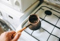 Man holding vintage jezve with freshly brewed coffee on the kitchen. Turkish pot over the oven Royalty Free Stock Photo