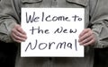 Man holding welcome to the new normal homemade sign with dark background Royalty Free Stock Photo