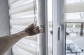 Man holding window handle on a plastic window with white fabric roller blinds in the living room. Close up on roll