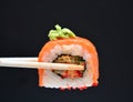 Man holding wooden chopsticks sushin, on top of wasabi sushi. dark background