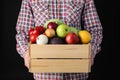 Man holding wooden crate filled with fresh vegetables and fruits against black background Royalty Free Stock Photo