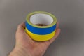 A man is holding yellow and blue duct tape in his hand. Reel of colored duct tape against the gray background. Selective focus. No