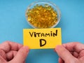 A man holding a yellow paper note with the words Vitamin D on it in his hands above a glass bowl with vitamin D3 softgels inside