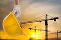 Man holding the yellow safety helmet at construction site with crane background silhouette Royalty Free Stock Photo