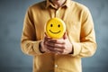 Man holding yellow smiley face on grey wall background, closeup. Customer experience or human emotional concept