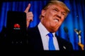 A man holds an android-smartphone that shows the logo for the google play store in front of the picture of Donald Trump