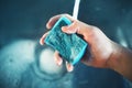 A man holds a blue sponge with foam in his hand over the kitchen sink, from the tap of which water flows. He was just washing the Royalty Free Stock Photo