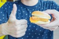 A man holds a burger in his hand and shows his thumb up. So good young man eats him delicious appetizing chicken burger