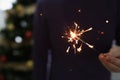 Man holds burning sparkler in dark room against backdrop of New Happy Christmas tree Royalty Free Stock Photo