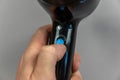 A man holds an electric hair dryer in his hand. His thumb turns on the ionization mode on the black electric device. Gray