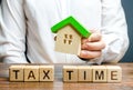 A man holds a figure of a house above the inscription Tax Time. Taxation, income tax. Declaring income, countering the shadow