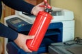 A man holds a fire extinguisher in his hands against the background of office equipment. Royalty Free Stock Photo