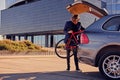 A man holds fixed bicycle near the car with open trunk.