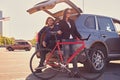 A man holds fixed bicycle near the car with open trunk.