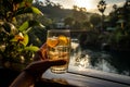 A man holds a glass with a cold summer drink in his hand, against the backdrop of a river and a tropical landscape.