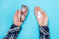 Man holds glasses for vision and container for contact lenses for the purpose of choosing what to use. Blue background