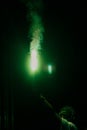 Man holds a green signal fire in outstretched hand on a black background