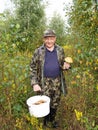 The man holds in hand a bucket with mushrooms in the wood