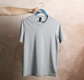 Man holds a hanger with blank gray t-shirt on brown background Royalty Free Stock Photo