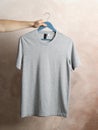 Man holds a hanger with blank gray t-shirt on brown background Royalty Free Stock Photo