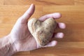 A man holds a heart shaped white potato in his open palm and fingers on a wooden cutting board background Royalty Free Stock Photo