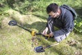 Man holds in his hand an object found in the ground. A metal detector and a shovel lie next to him. Royalty Free Stock Photo