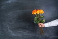 A man holds in his hand three orange roses against the background of a chalk board