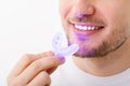 A man holds in his hand an ultraviolet lamp for home teeth whitening. A snow-white smile after bleaching.