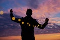 Man holds in his hands a garland lights on the background of colorful sky on sunrise Royalty Free Stock Photo