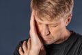 A man holds his hands on his head on blue background. Headache or migraine.