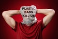 The man holds his head in his hands, suffocating in a plastic bag. Red background. The inscription Plastic bags kill us. Concept