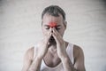 The man holds his nose and sinus area with fingers in obvious pabvious pain from a head ache in the front forehead area.