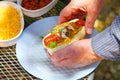 Man holds hot dog with cheese, relish, onions