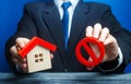 A man holds a house and the red prohibition symbol NO. Bank refuses to provide a mortgage loan. Housing problems. Confiscation Royalty Free Stock Photo