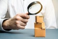 A man holds a magnifying glass above the boxes. Examination of goods for the presence of contraband, prohibited goods, defects.