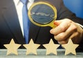 A man holds a magnifying glass over four stars. The evaluation of visitors. Quality level, good service. Best customer rating.