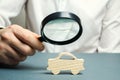 A man holds a magnifying glass over a miniature wooden car. The estimated cost of the auto. Analysis and technical inspection of