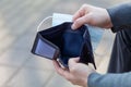 Man holds a medical mask and empty wallet without money. Bankruptcy and unemployment resulting from the global coronavirus