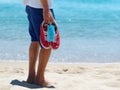 Man holds Medical Mask, Red Sneakers in Sandy Tropical Beach. Royalty Free Stock Photo