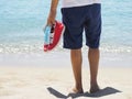 Man holds Medical Mask, Red Sneakers in Sandy Tropical Beach. Royalty Free Stock Photo