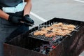 A man holds a mesh for a barbecue. Burning coals in the grill. He is wearing black medical gloves and an apron.Picnic in the city