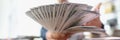 Man holds money fan in hands sitting at table with banknotes