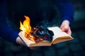 A man holds an open book in his hands, the pages of which burn with a bright flame